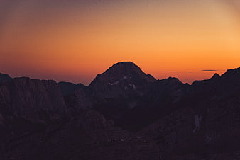 Silhouette of mountain peaks against vibrant orange sunset sky