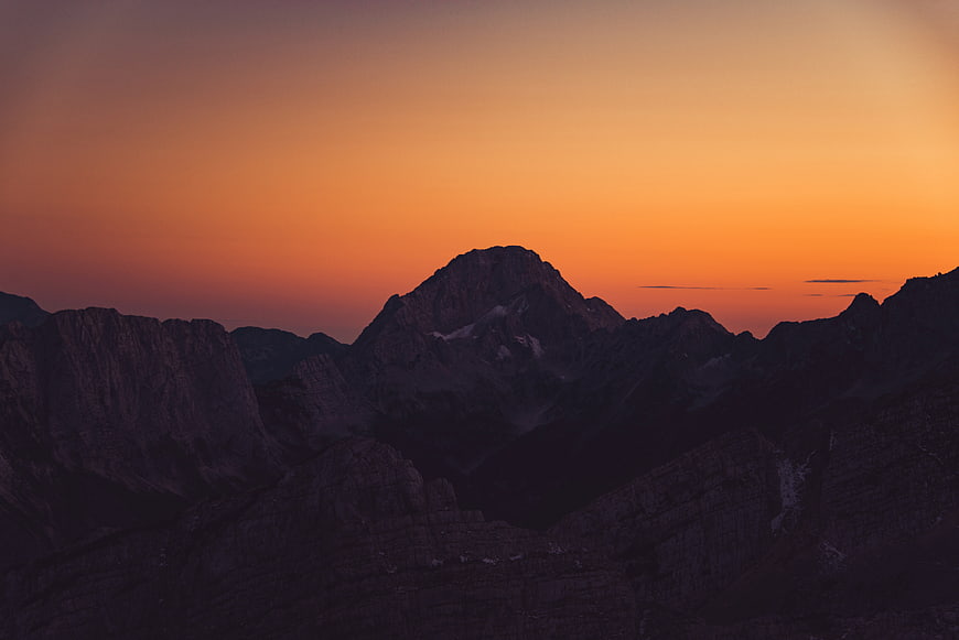 Silhouette of mountain peaks against vibrant orange sunset sky