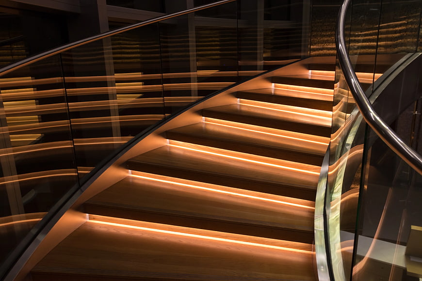 Modern wooden staircase with warm LED lighting and glass railing