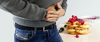 Man holding stomach in pain next to stack of pancakes