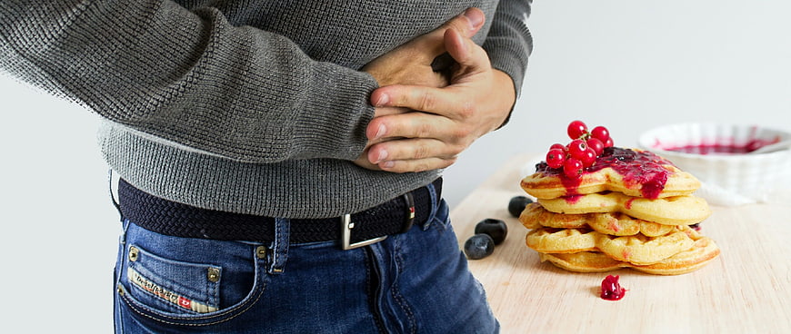 Man holding stomach in pain next to stack of pancakes