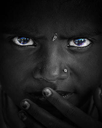 Close-up portrait of a young girl with blue eyes and hand over mouth
