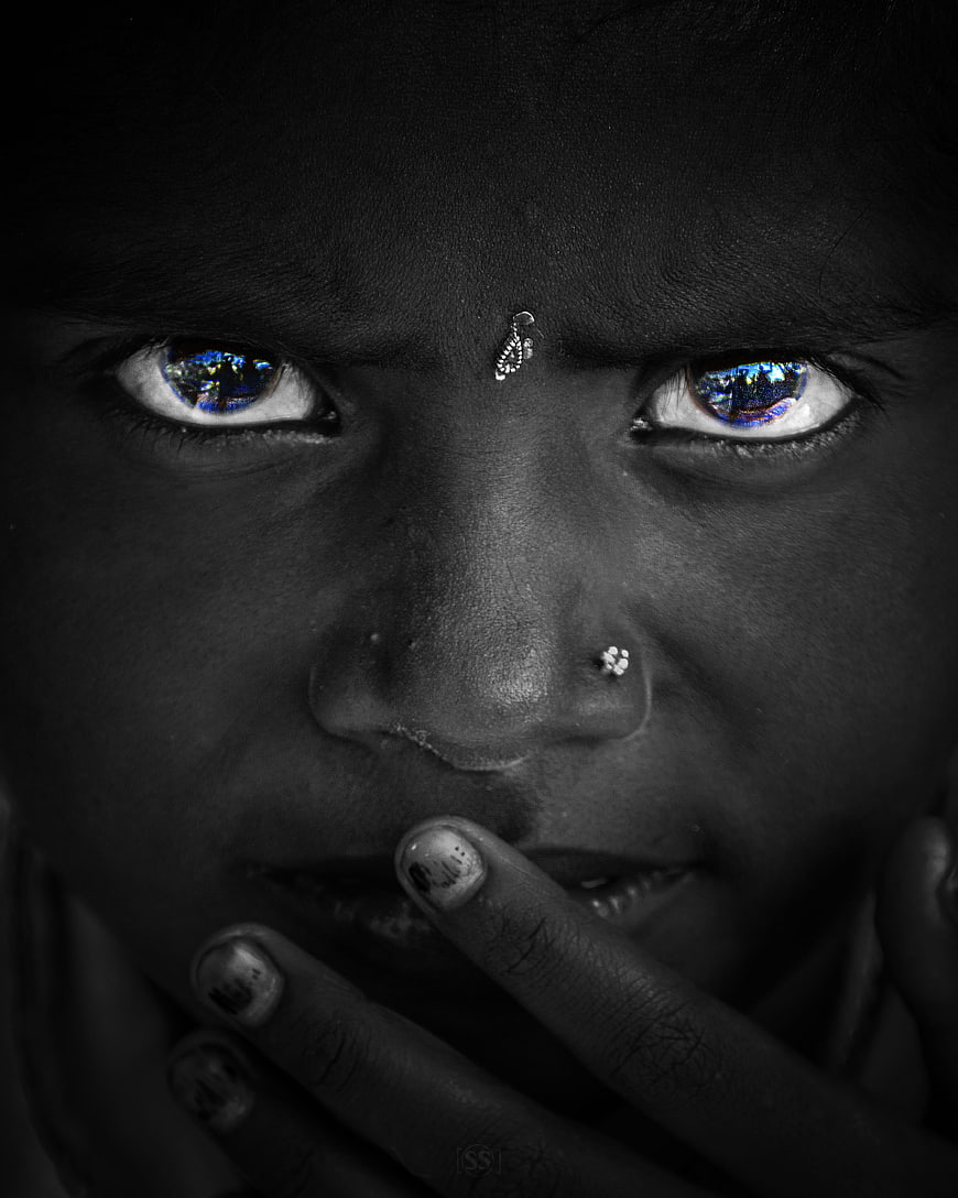 Close-up portrait of a young girl with blue eyes and hand over mouth