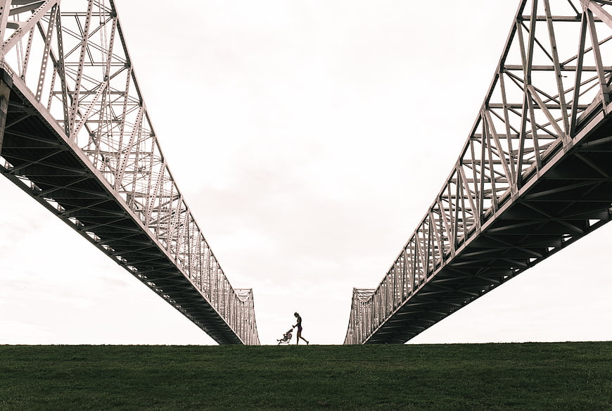 Woman pushing stroller under large steel bridge structure