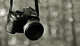 Black and White Nikon DSLR Camera Hanging Against Blurred Forest Bokeh