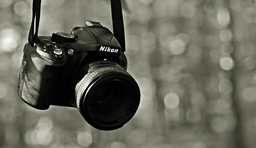 Black and White Nikon DSLR Camera Hanging Against Blurred Forest Bokeh