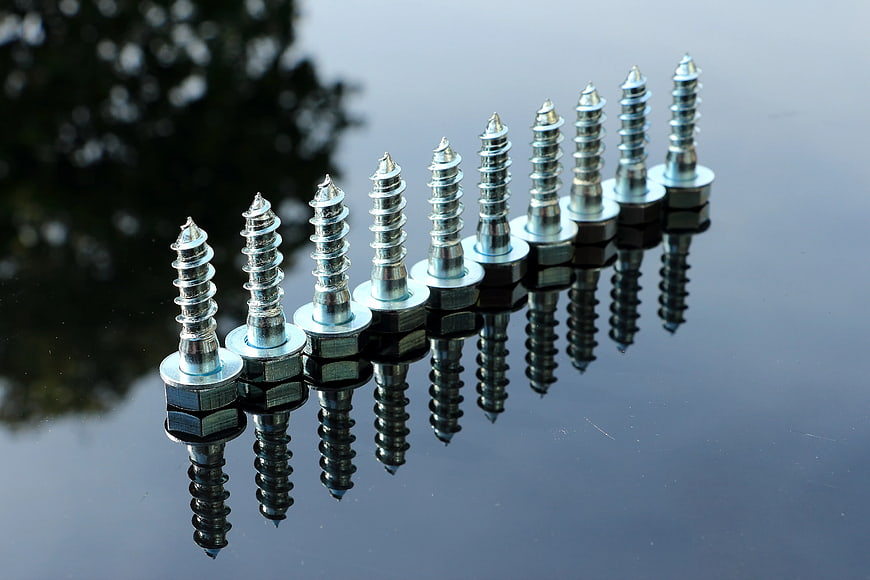 Row of silver screws with reflections on black surface