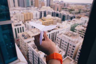 Hand holding paper airplane over blurred city skyline