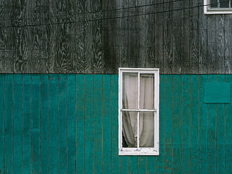 Weathered wooden wall with white window and teal paint