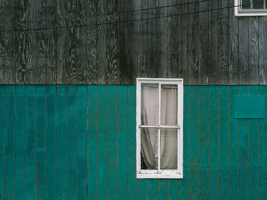 Weathered wooden wall with white window and teal paint