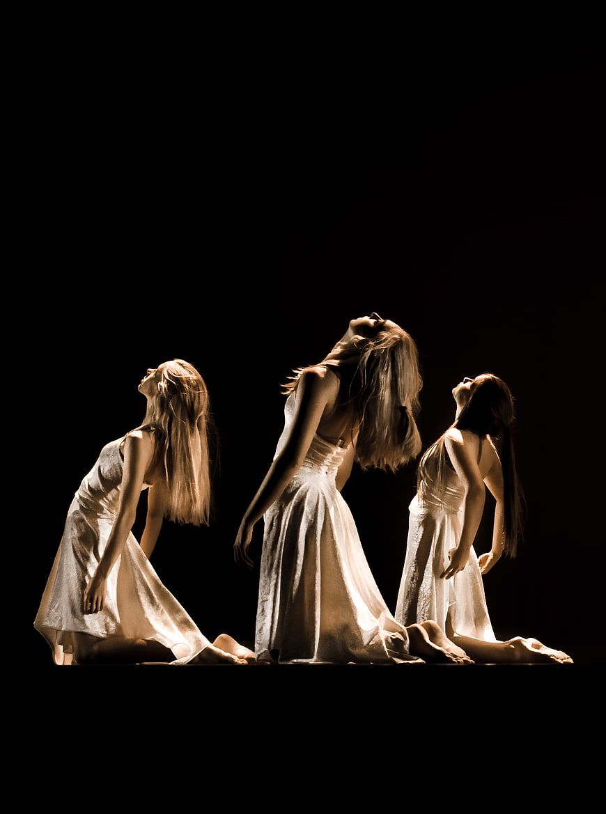 Three female dancers in white dresses performing modern dance on stage