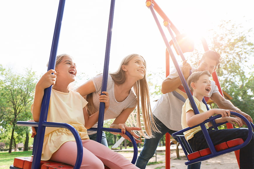 Happy family playing on swings in sunny park