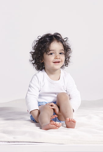 Cute toddler girl with curly hair sitting on white bed