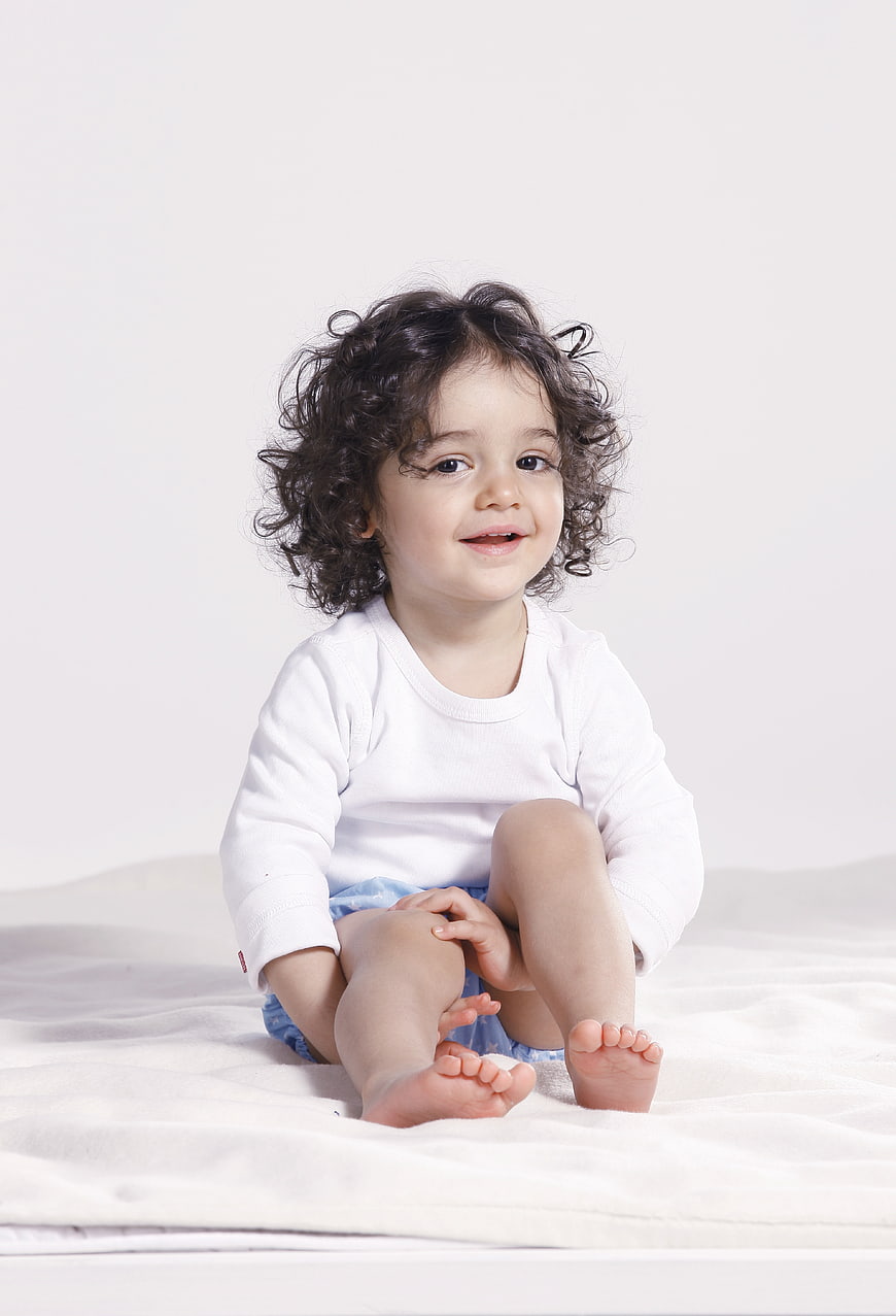 Cute toddler girl with curly hair sitting on white bed