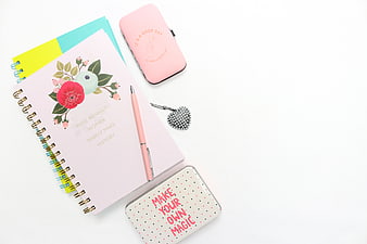 Flat lay of pink floral notebook, stationery, and accessories on white background