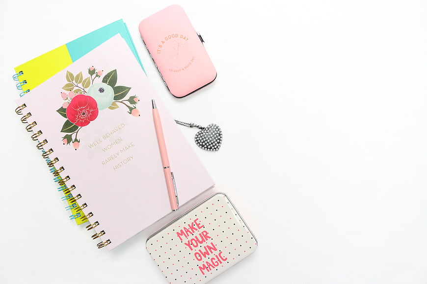 Flat lay of pink floral notebook, stationery, and accessories on white background