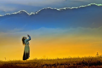 Woman in field reaching up to dramatic sunset sky