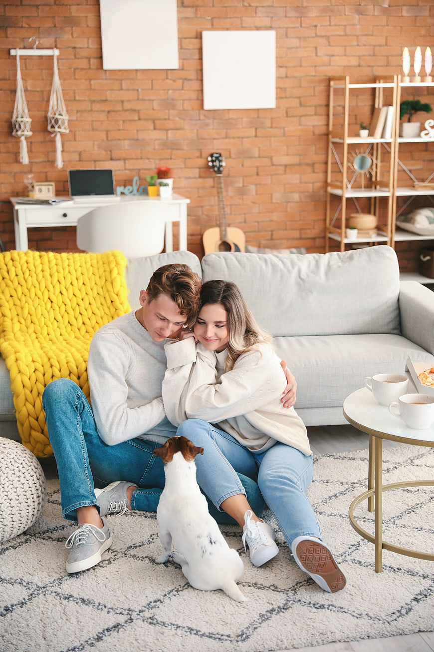 Happy young couple hugging on living room floor with dog
