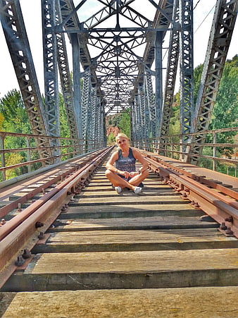 Woman sitting on railway tracks of old metal bridge