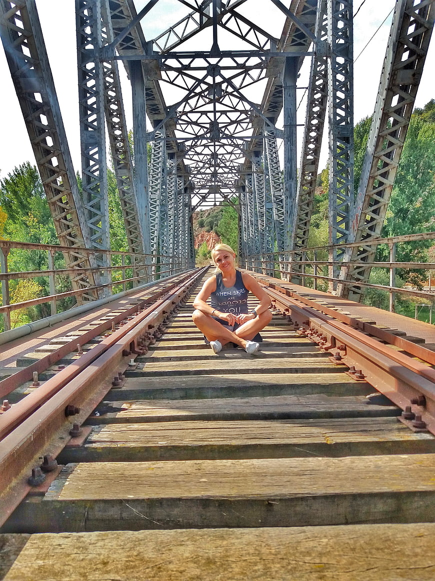 Woman sitting on railway tracks of old metal bridge