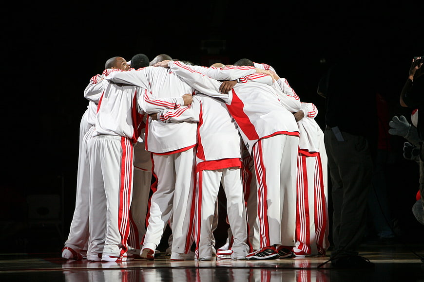 Professional basketball team huddle on court in white and red uniforms