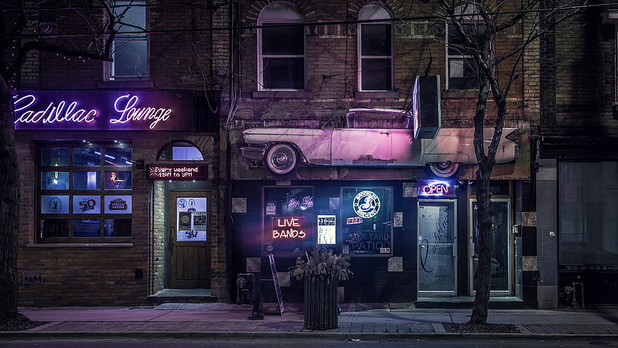 Neon-lit Cadillac Lounge bar exterior at night with vintage car mural
