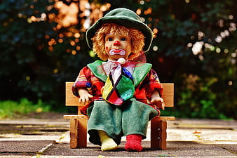 Sad clown doll sitting on a miniature wooden bench outdoors