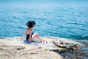 Woman in black swimsuit and hat relaxing on rocky shore
