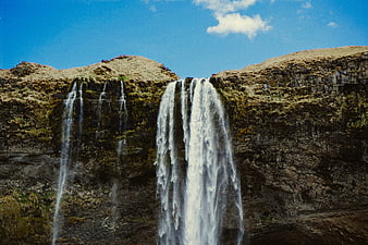 Mossy Waterfall Cascading Down Rocky Cliff Under Blue Sky