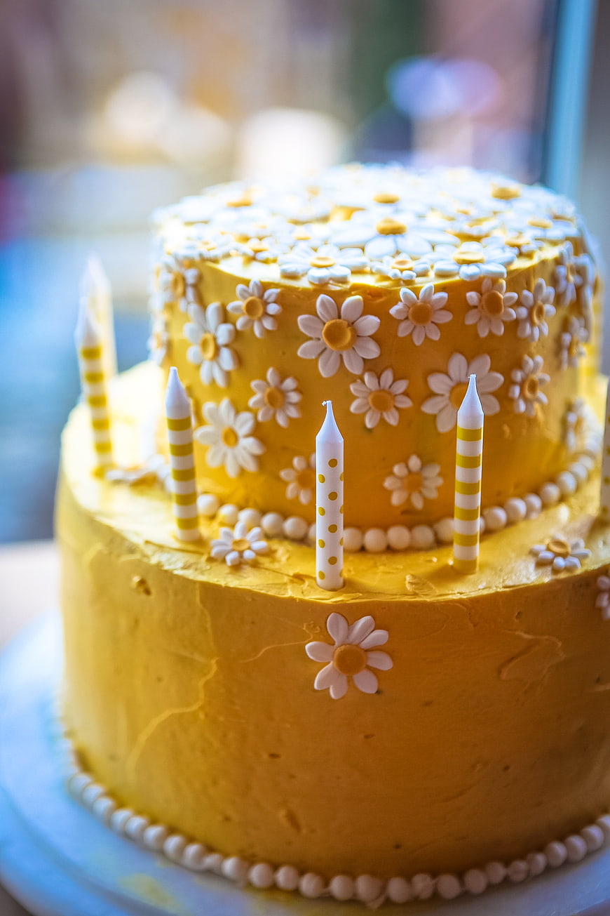 Two-Tier Yellow Birthday Cake With White Daisy Decorations And Candles