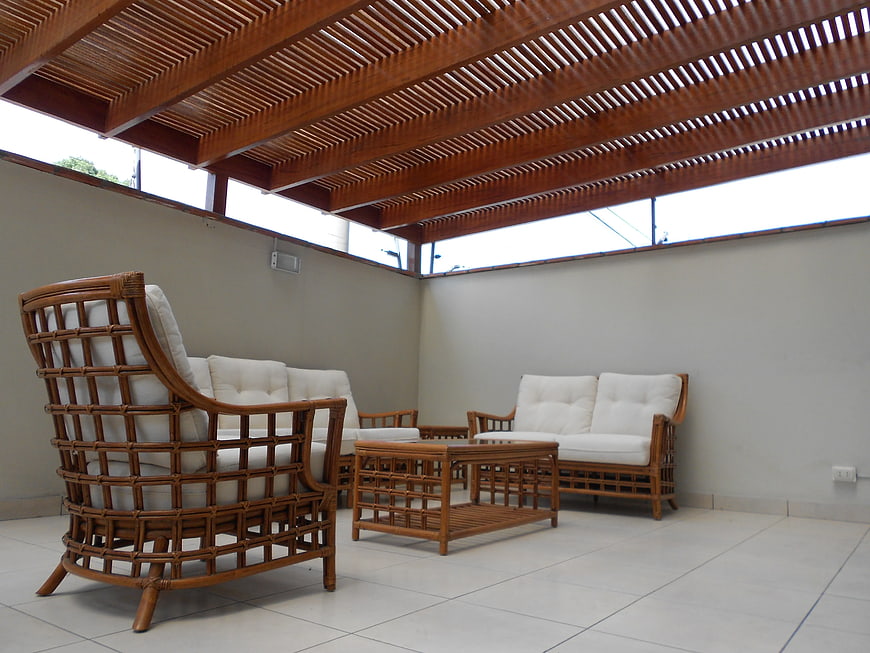 Rattan furniture set with white cushions under wooden pergola