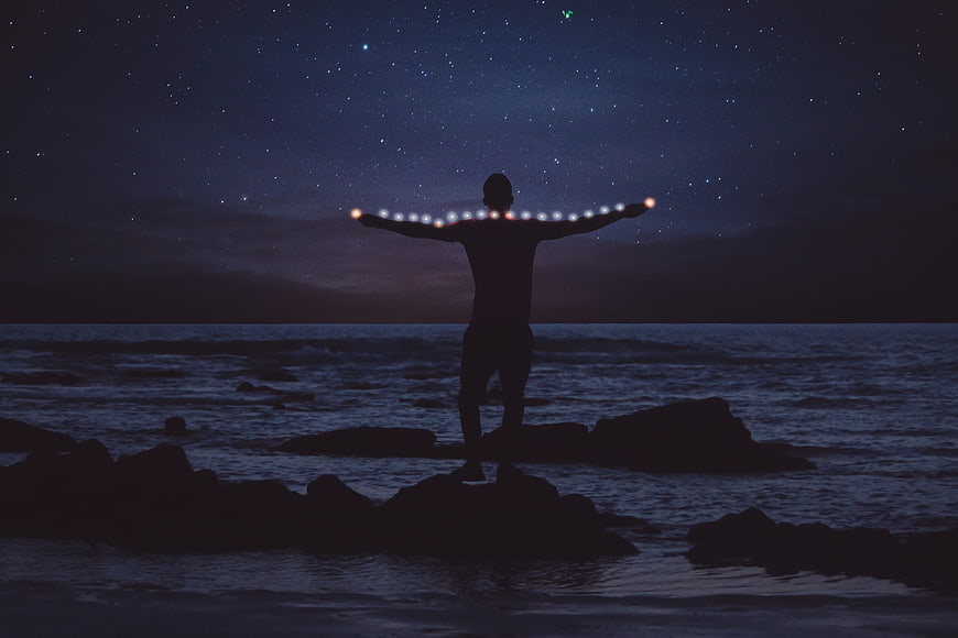 Silhouette of Man with LED Lights on Rocky Coast at Night