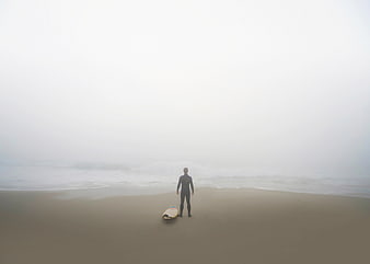 Lone Surfer Standing on Foggy Beach with Surfboard