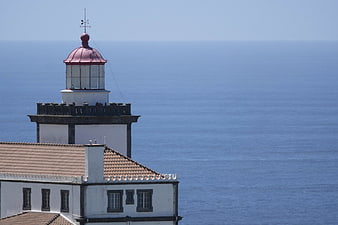 White Lighthouse with Red Roof Overlooking Blue Ocean