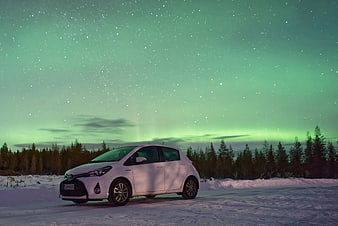 White car parked in snow under green aurora borealis night sky