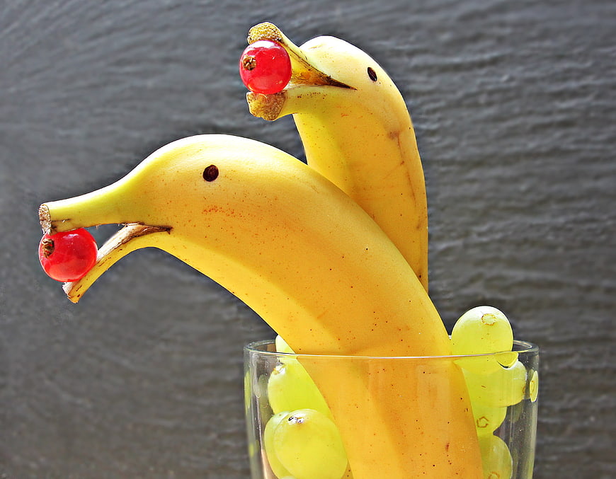 Creative banana dolphins with cranberries and grapes in glass