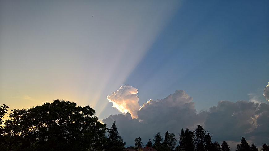 Dramatic Sun Rays Breaking Through Storm Clouds Over Trees