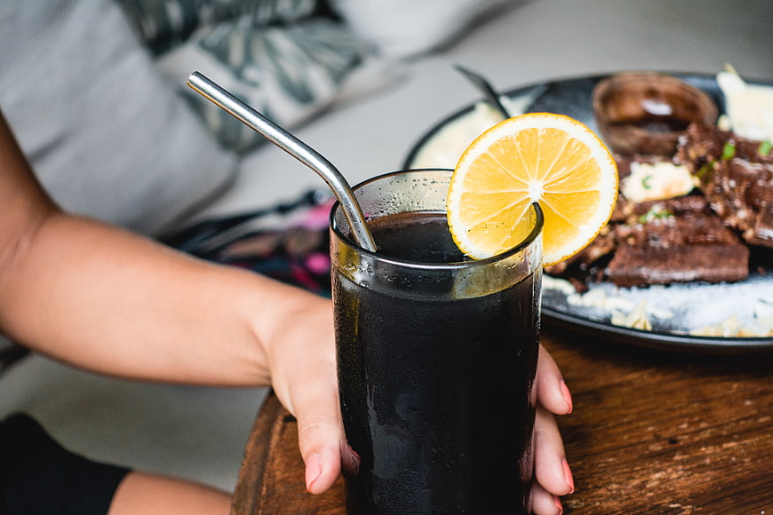 Hand holding iced black lemonade with lemon slice