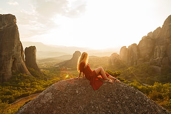Woman in Red Dress Sitting on Rock Overlooking Meteora at Sunset