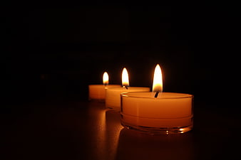Three lit tea light candles glowing warmly against a dark background