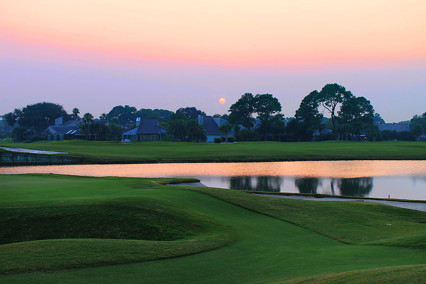 Sunset Over Manicured Golf Course With Water Hazard And Residential Homes