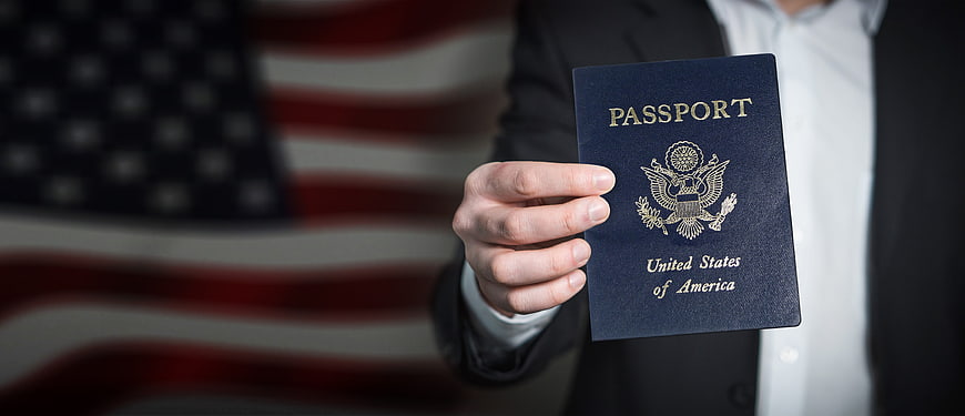 Hand Holding US Passport in Front of American Flag