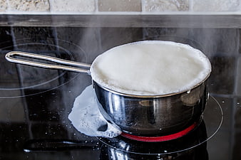 Boiling milk overflowing from stainless steel pot on electric stove