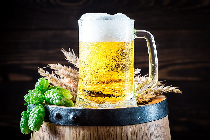 Cold Draft Beer Mug on Wooden Barrel with Hops and Wheat