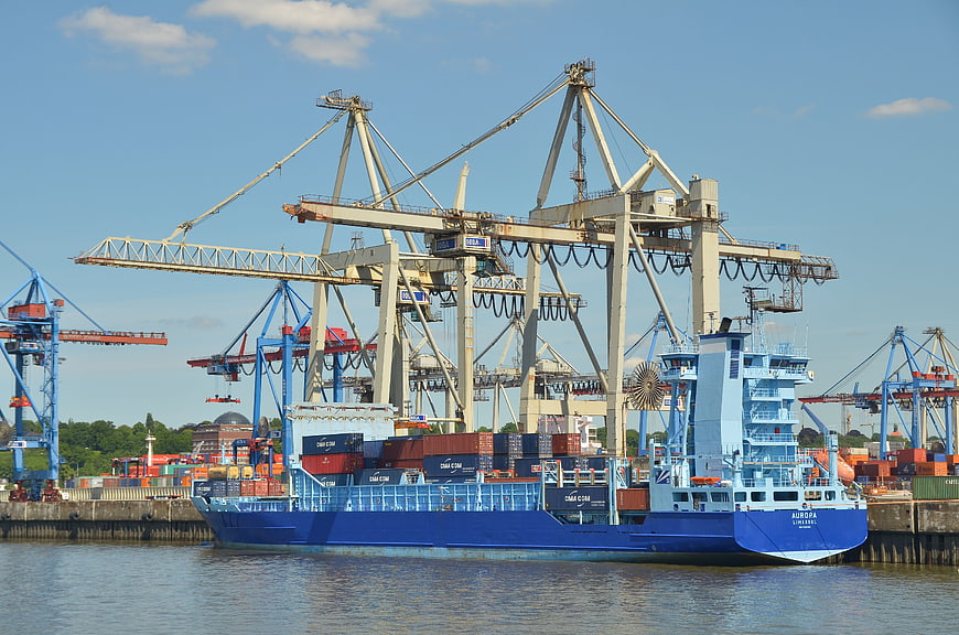 Blue container ship docked at busy industrial port with cranes