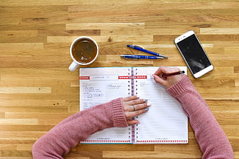 Woman writing in notebook on wooden desk with coffee and smartphone