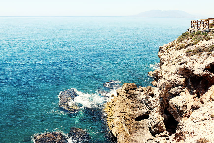 Sunny coastal cliff with turquoise sea and wooden railing