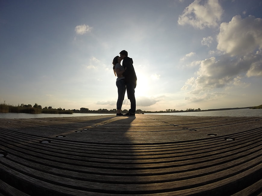 Romantic couple kissing silhouette on wooden pier at sunset