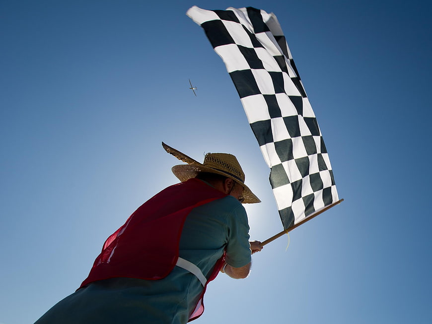 Man in straw hat waving checkered flag at air race finish line