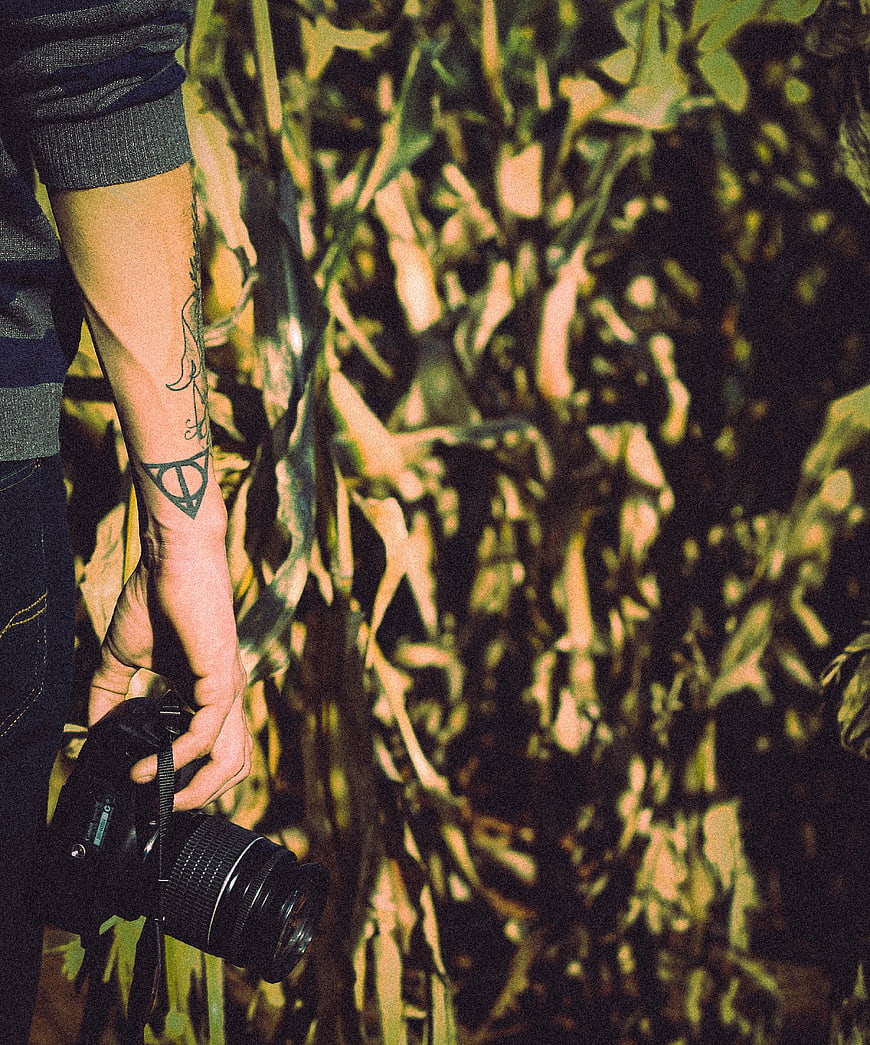 Man with tattoo holding camera in cornfield